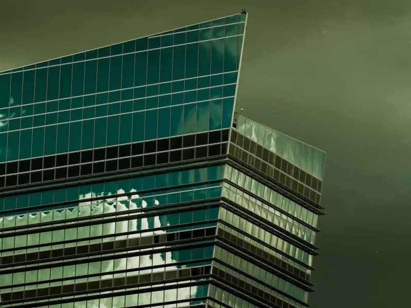 An angular glass office tower reflecting cloud against a dark storm sky