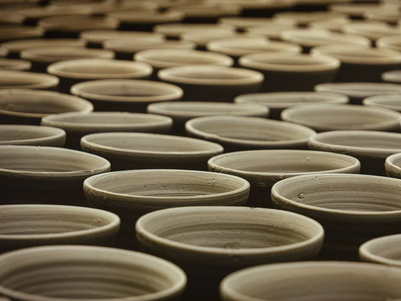 Rows of handmade clay cups drying in a pottery workshop, lit in warm amber
