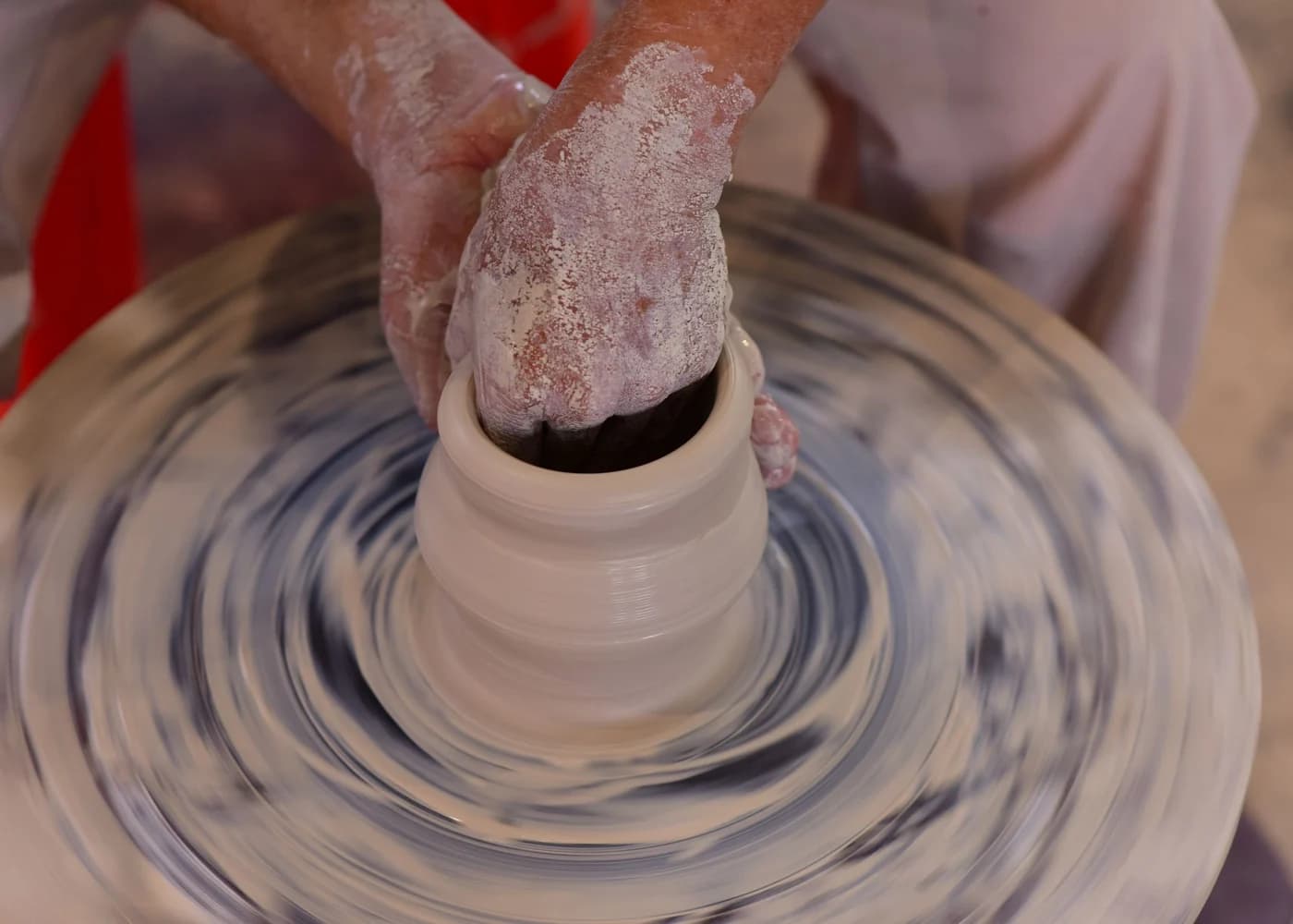 A potter's hands shaping wet clay on a wheel in a sunlit workshop