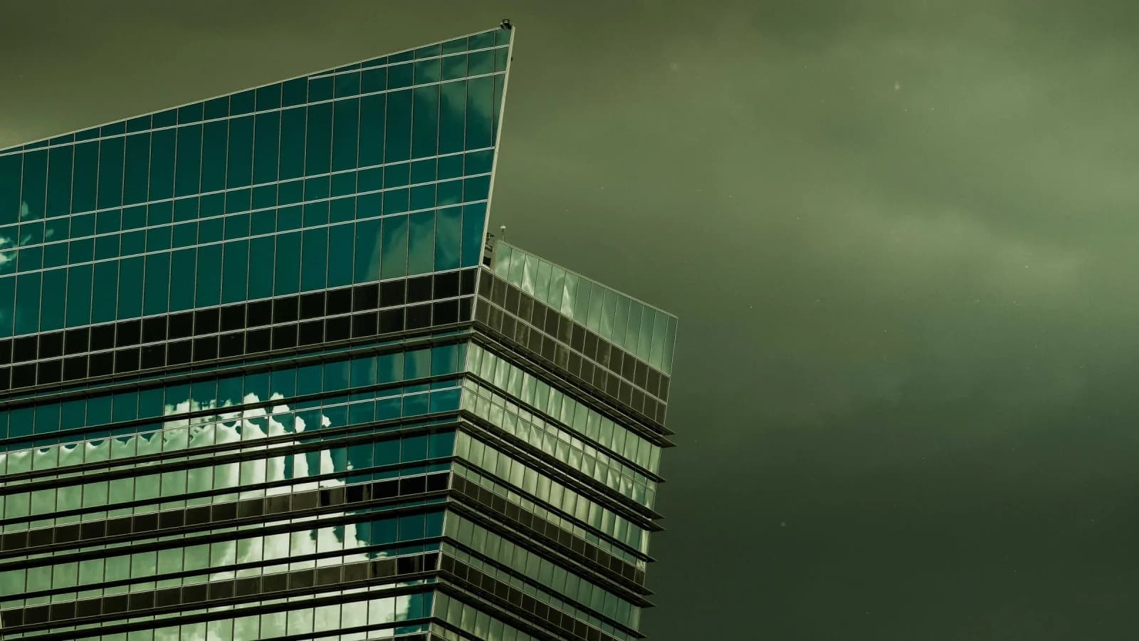 An angular glass office tower reflecting cloud against a dark storm sky