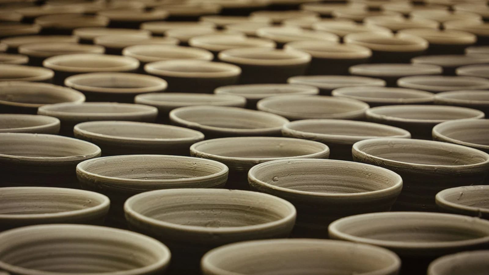Rows of handmade clay cups drying in a pottery workshop, lit in warm amber