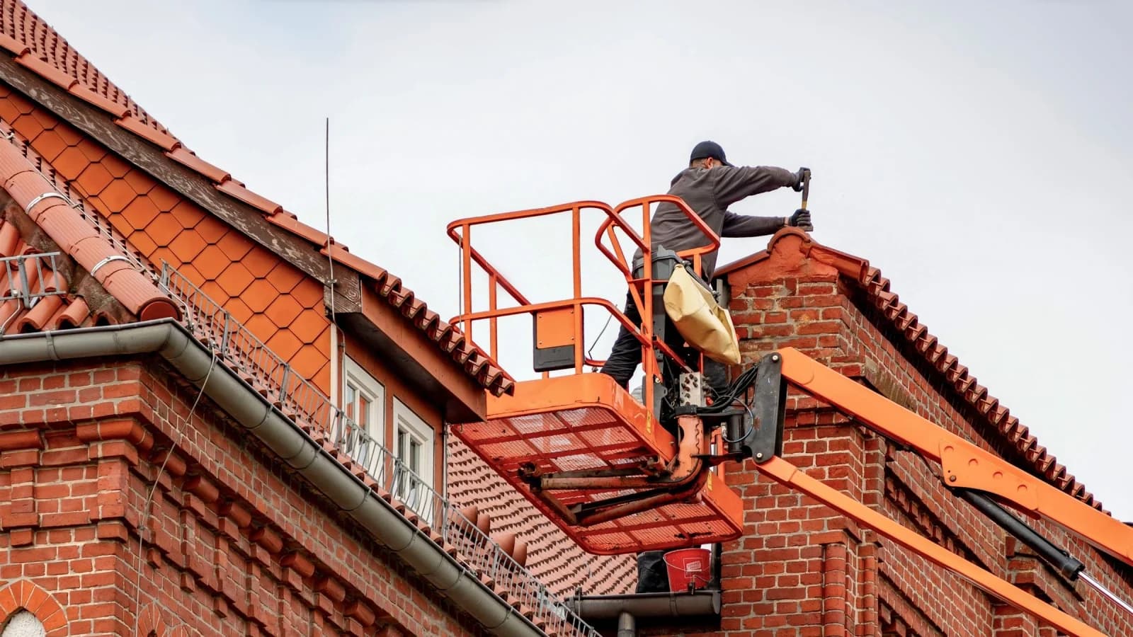 A roofer working from a lift platform against the brick gables and tiled roof of a house